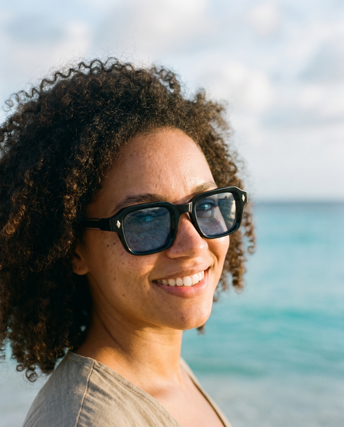Woman wearing KENEPA black square sunglasses with blue lens on a Curacao beach